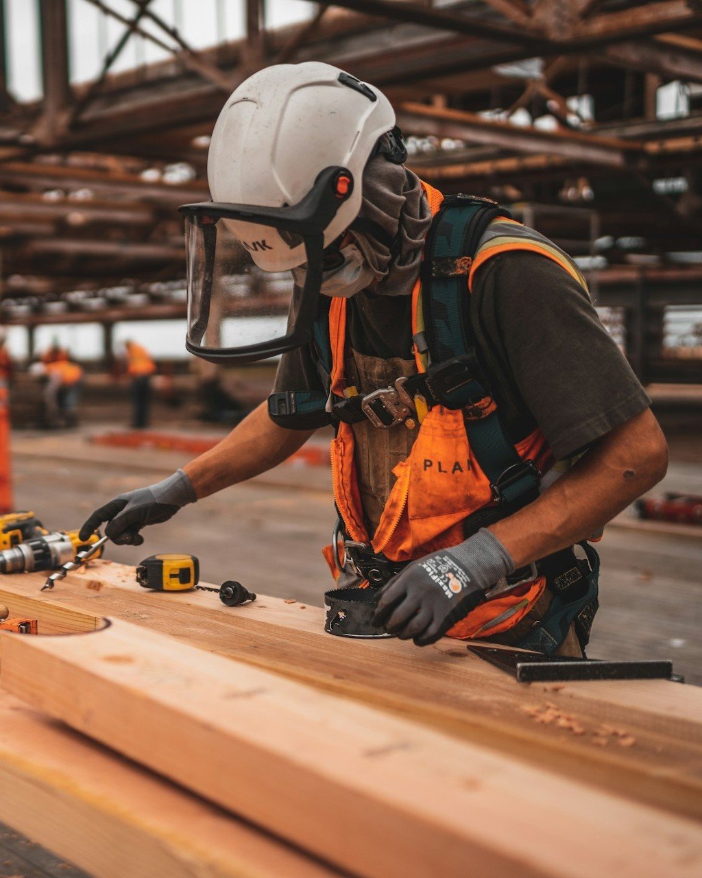 Skilled carpenter wearing full PPE and safety face shield working on timber framing at a construction site, representing Smart Agnes's civil and fit-out expertise.