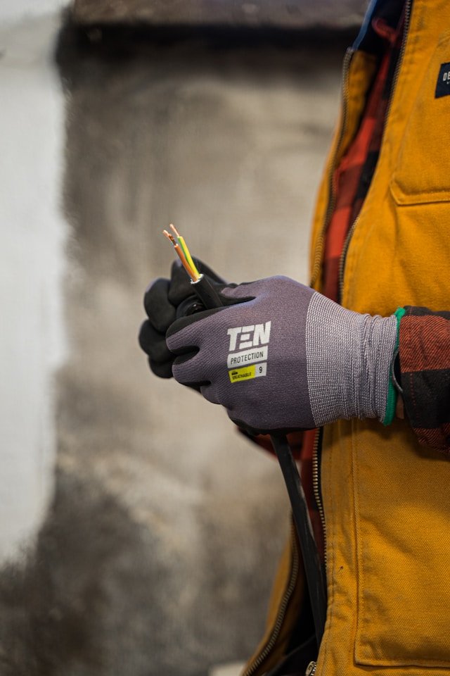 A close-up of a professional electrician in protective gear holding stripped electrical wiring, showcasing Smart Agnes’s highly skilled technical staff and electrical maintenance services in Qatar.